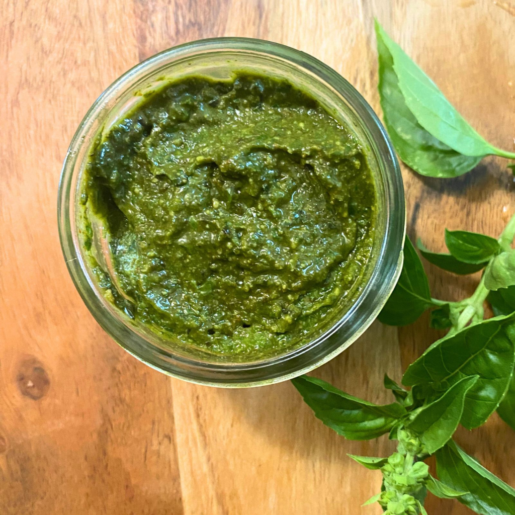 Small open jar of pesto with basil leaves nest to it