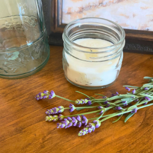 Small white soy candle in jar with lavender sprigs, a photo frame, and a glass vase around it