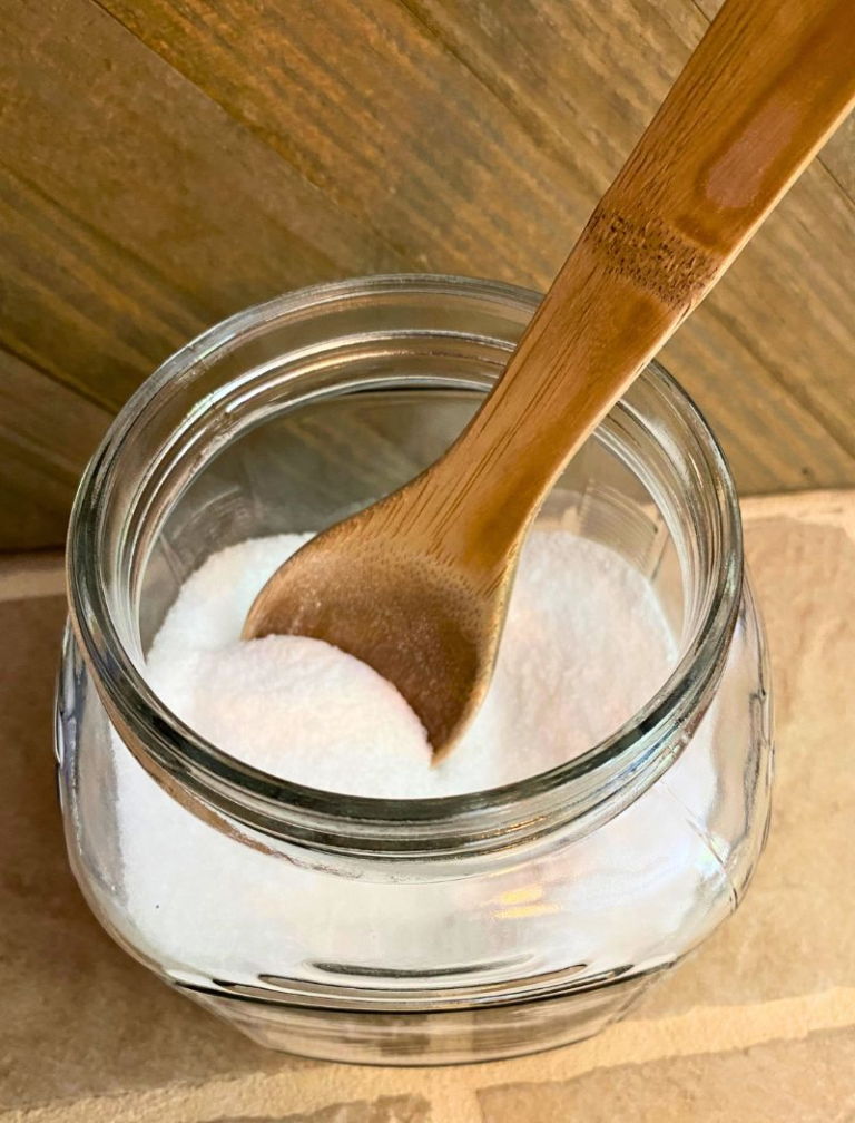 Large clear glass jar with powdered laundry scent booster and a wooden spoon in it