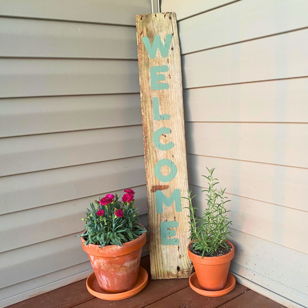 DIY welcome porch sign on porch next to flower pots