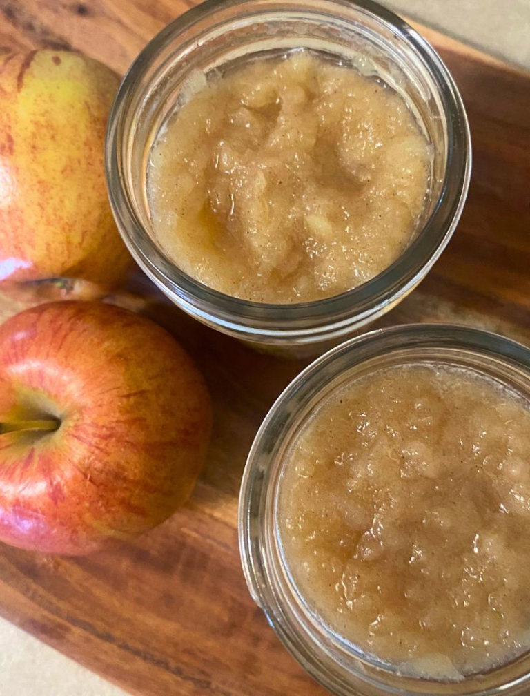 Homemade applesauce in mason jars next to red apples
