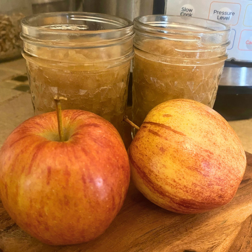 Homemade applesauce in mason jars next to red apples and an Instant Pot