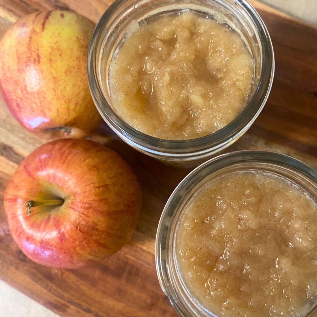 Homemade applesauce in mason jars next to red apples