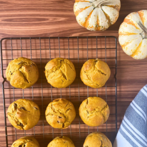 Sourdough pumpkin muffins on cooling rack next to small pumpkins