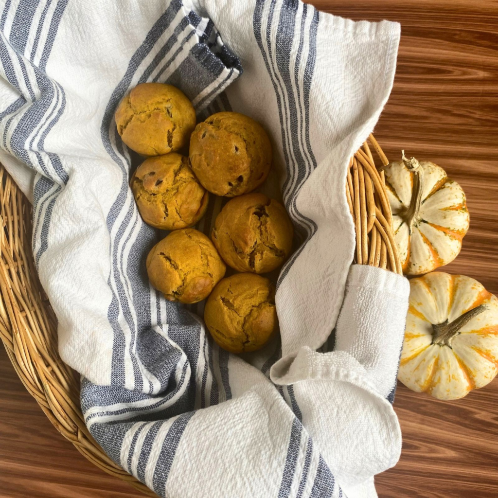 Sourdough pumpkin muffins in basket with towel next to small pumpkins